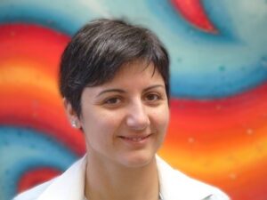 Head and shoulders image of Dr Theodosia Stratoudaki. She is standing in front of a wall with red and blue waves painted on it.